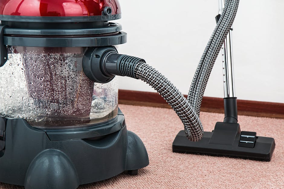 A person operating a yellow industrial carpet cleaning machine, with hands on the handle and control panel, positioned on a patterned, beige and green rug in a room with warm lighting, indicating surf